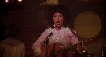 Movie still from “Making Love” (1982), directed by Arthur Hiller – A woman in a cowboy hat holding a guitar; Close Up shot, Over the shoulder angle