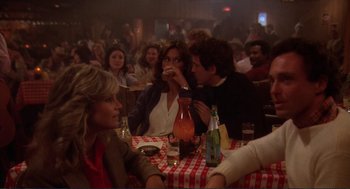Movie still from “Making Love” (1982), directed by Arthur Hiller – A group of people sitting at a table with drinks; Medium shot, Over the shoulder angle