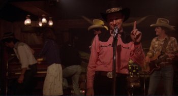 Movie still from “Making Love” (1982), directed by Arthur Hiller – A man wearing a cowboy hat holding a microphone; Medium shot, Low angle