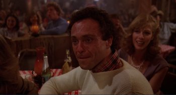 Movie still from “Making Love” (1982), directed by Arthur Hiller – A person sitting at a table in front of other people; Close Up shot, Over the shoulder angle