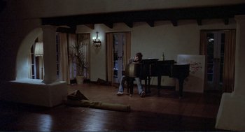 Movie still from “Making Love” (1982), directed by Arthur Hiller – A man sitting at a table in front of a piano; Wide shot, High angle
