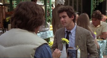 Movie still from “Making Love” (1982), directed by Arthur Hiller – A man in a suit and tie holding a yellow flower; Medium shot, Over the shoulder angle