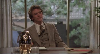 Movie still from “Making Love” (1982), directed by Arthur Hiller – A man sitting at a table in a suit and tie; Medium shot, Over the shoulder angle