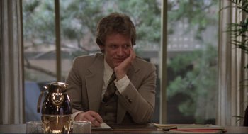 Movie still from “Making Love” (1982), directed by Arthur Hiller – A man sitting at a table in front of a window looking pensive; Medium shot, Over the shoulder angle