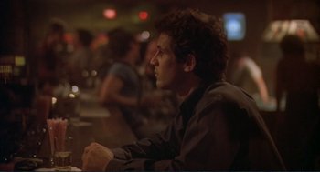 Movie still from “Making Love” (1982), directed by Arthur Hiller – A man sitting at a table in front of other people; Close Up shot, Over the shoulder angle