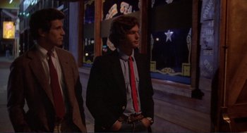 Movie still from “Making Love” (1982), directed by Arthur Hiller – A man in a suit and a red tie standing next to another man in a suit; Medium shot, Low angle