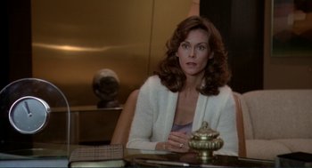 Movie still from “Making Love” (1982), directed by Arthur Hiller – A woman sitting at a table in front of a gold statue; Medium shot, Over the shoulder angle
