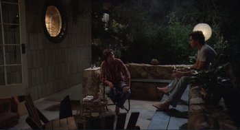 Movie still from “Making Love” (1982), directed by Arthur Hiller – A man sitting on top of a chair next to a fire pit; Wide shot, High angle
