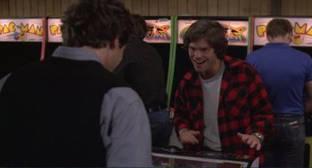 Movie still from “Making Love” (1982), directed by Arthur Hiller – A man sitting at a table talking to another man; Medium shot, Over the shoulder angle