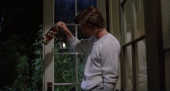 Movie still from “Making Love” (1982), directed by Arthur Hiller – A man holding a bottle of beer in front of a window; Medium shot, Low angle