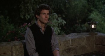 Movie still from “Making Love” (1982), directed by Arthur Hiller – A man sitting on top of a stone wall; Medium shot, Over the shoulder angle