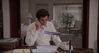 Movie still from “Making Love” (1982), directed by Arthur Hiller – A man sitting at a desk talking on a phone; Medium shot, Low angle