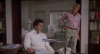 Movie still from “Making Love” (1982), directed by Arthur Hiller – A man sitting in front of a microphone while another man stands next to him; Medium shot, Low angle