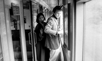 Movie still from “Man Bites Dog” (1992), directed by Benoît Poelvoorde – A man and a woman standing on a train looking out a window; Medium shot, Over the shoulder angle