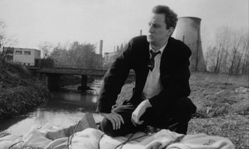 Movie still from “Man Bites Dog” (1992), directed by Benoît Poelvoorde – A black and white photo of a man in a suit and tie; Medium shot, Low angle