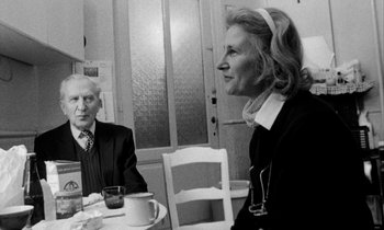 Movie still from “Man Bites Dog” (1992), directed by Benoît Poelvoorde – An older man and a woman sitting at a table; Medium shot, Over the shoulder angle