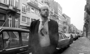 Movie still from “Man Bites Dog” (1992), directed by Benoît Poelvoorde – A black and white photo of a man standing in the street; Medium shot, Low angle