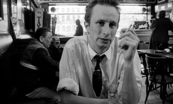 Movie still from “Man Bites Dog” (1992), directed by Benoît Poelvoorde – A man sitting at a table with a cigarette in his mouth; Close Up shot, Low angle