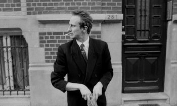 Movie still from “Man Bites Dog” (1992), directed by Benoît Poelvoorde – A black and white photo of a man in a suit and tie; Medium shot, Low angle