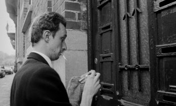 Movie still from “Man Bites Dog” (1992), directed by Benoît Poelvoorde – A black and white photo of a man smoking a cigarette; Medium shot, Low angle