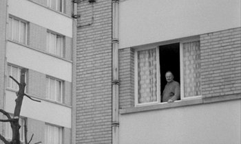 Movie still from “Man Bites Dog” (1992), directed by Benoît Poelvoorde – An older man looking out of a window; Wide shot, High angle