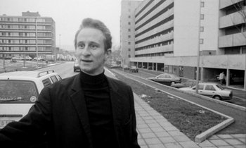 Movie still from “Man Bites Dog” (1992), directed by Benoît Poelvoorde – A black and white photo of a man standing on the side of the street; Medium shot, Low angle