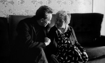 Movie still from “Man Bites Dog” (1992), directed by Benoît Poelvoorde – An older woman sitting next to a younger man; Medium shot, High angle