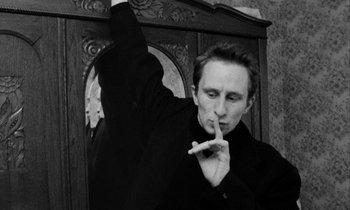 Movie still from “Man Bites Dog” (1992), directed by Benoît Poelvoorde – A man in a black shirt is putting a finger to his mouth; Close Up shot, Low angle