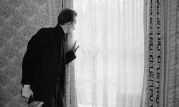 Movie still from “Man Bites Dog” (1992), directed by Benoît Poelvoorde – A black and white photo of a man looking out of a window; Medium shot, Low angle
