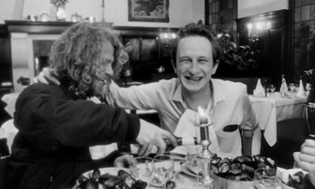 Movie still from “Man Bites Dog” (1992), directed by Benoît Poelvoorde – Two people sitting at a dinner table with a candle in their hand; Medium shot, High angle