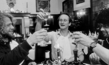 Movie still from “Man Bites Dog” (1992), directed by Benoît Poelvoorde – A group of people sitting at a table drinking wine; Medium shot, Low angle