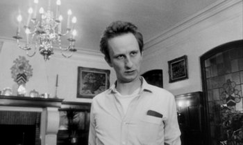 Movie still from “Man Bites Dog” (1992), directed by Benoît Poelvoorde – A black - and - white photo of a man standing in front of a fireplace; Close Up shot, Low angle