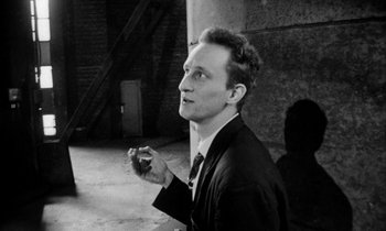 Movie still from “Man Bites Dog” (1992), directed by Benoît Poelvoorde – A black and white photo of a man smoking a cigarette; Close Up shot, High angle