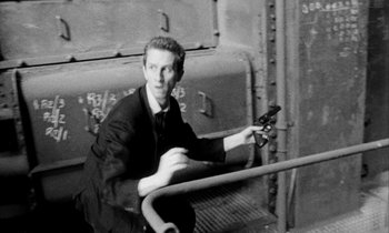 Movie still from “Man Bites Dog” (1992), directed by Benoît Poelvoorde – A black and white photo of a man sitting on a bench; Medium shot, High angle