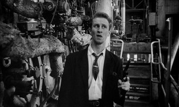 Movie still from “Man Bites Dog” (1992), directed by Benoît Poelvoorde – A black and white photo of a man in a suit and tie holding a wrench; Medium shot, Low angle