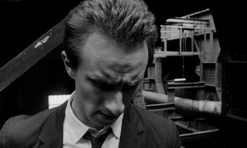 Movie still from “Man Bites Dog” (1992), directed by Benoît Poelvoorde – A black and white photo of a man in a suit and tie; Close Up shot, High angle
