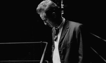 Movie still from “Man Bites Dog” (1992), directed by Benoît Poelvoorde – Black and white photograph of a man wearing a suit and tie; Close Up shot, Low angle