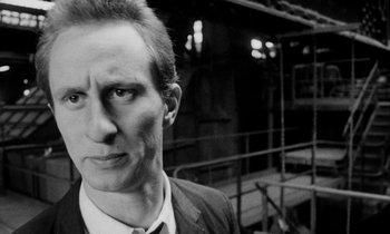 Movie still from “Man Bites Dog” (1992), directed by Benoît Poelvoorde – A black and white photo of a man in a suit and tie; Close Up shot, Low angle