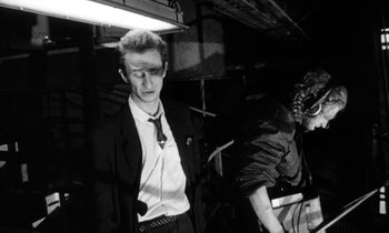 Movie still from “Man Bites Dog” (1992), directed by Benoît Poelvoorde – A black and white photo of a man in a suit and tie; Medium shot, Low angle