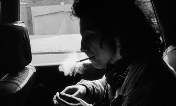 Movie still from “Man Bites Dog” (1992), directed by Benoît Poelvoorde – A man smoking a cigarette while sitting in a car; Close Up shot, Low angle