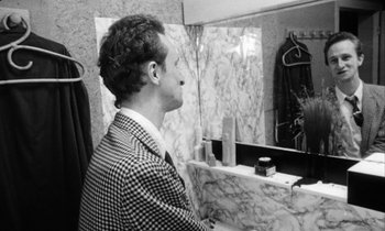 Movie still from “Man Bites Dog” (1992), directed by Benoît Poelvoorde – A black and white photo of a man looking at himself in the mirror; Medium shot, Over the shoulder angle