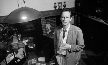 Movie still from “Man Bites Dog” (1992), directed by Benoît Poelvoorde – A black and white photo of a man standing in a living room; Medium shot, Low angle
