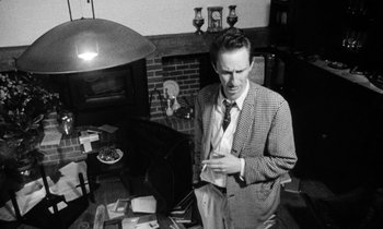 Movie still from “Man Bites Dog” (1992), directed by Benoît Poelvoorde – A black and white photo of a man standing in a living room; Medium shot, High angle