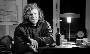 Movie still from “Man Bites Dog” (1992), directed by Benoît Poelvoorde – Black and white photograph of a man sitting at a table with a bottle of alcohol; Close Up shot, Low angle
