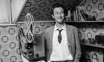 Movie still from “Man Bites Dog” (1992), directed by Benoît Poelvoorde – A black and white photo of a man in a suit and tie; Medium shot, High angle