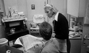 Movie still from “Man Bites Dog” (1992), directed by Benoît Poelvoorde – Two people in a kitchen looking at a newspaper; Medium shot, Over the shoulder angle