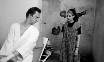 Movie still from “Man Bites Dog” (1992), directed by Benoît Poelvoorde – A man and a woman standing next to each other in a room; Medium shot, Over the shoulder angle