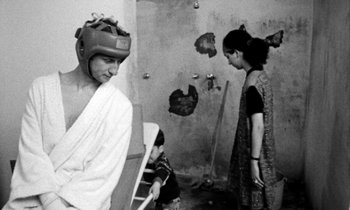 Movie still from “Man Bites Dog” (1992), directed by Benoît Poelvoorde – A man and a woman in a room with a broken wall in the background; Medium shot, Over the shoulder angle