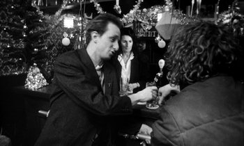 Movie still from “Man Bites Dog” (1992), directed by Benoît Poelvoorde – A black and white photo of a man at a party; Medium shot, Over the shoulder angle