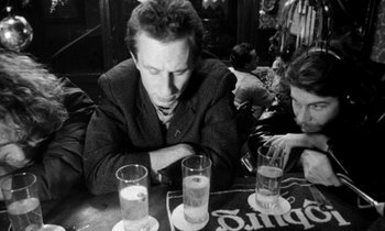 Movie still from “Man Bites Dog” (1992), directed by Benoît Poelvoorde – A black and white photo of a man sitting at a table; Medium shot, Low angle